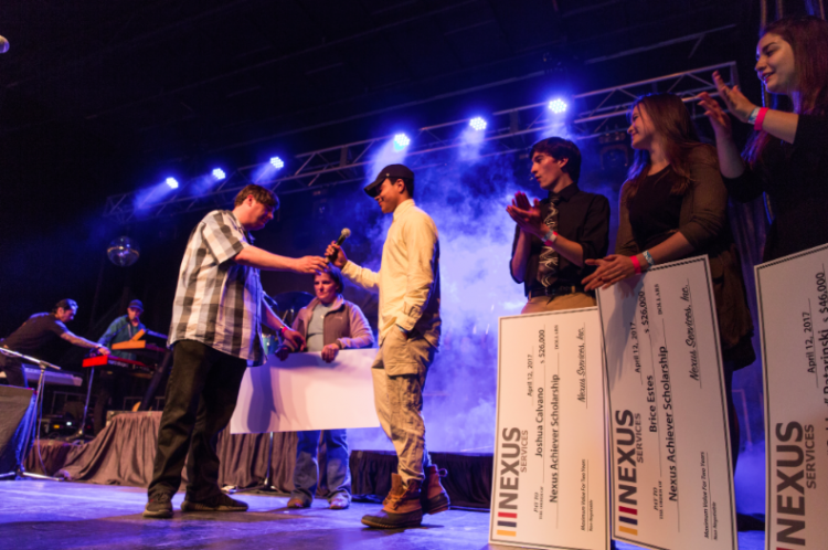 Mike Donovan, CEO y presidente de Nexus Services, presenta a los ganadores de la beca Nexus con cheques antes de que Nate Ruess suba al escenario en un concierto comunitario en Verona, Virginia.