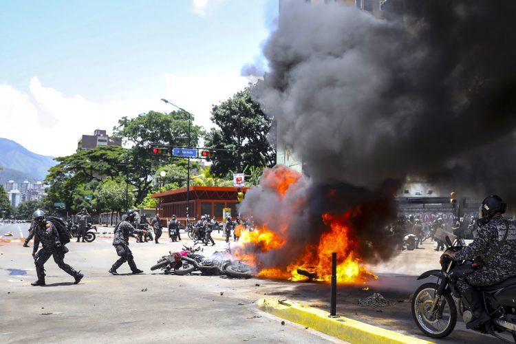 Agentes de la Guardia Nacional Bolivariana lanzan motocicletas usadas por periodistas a un incendio causado por una explosión el pasado, domingo 30 de julio de 2017, en inmediaciones de la Plaza Altamira de Caracas (Venezuela). Un agente resultó hoy herido tras la explosión de dos motos de la Policía Nacional Bolivariana (PNB) y otra de un civil, en las inmediaciones de una protesta ciudadana en Caracas contra las elecciones a la Asamblea Nacional Constituyente, convocada por el presidente venezolano, Nicolás Maduro. EFE/Miguel Gutiérrez