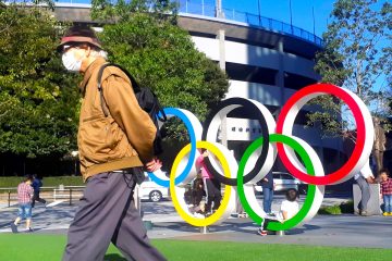 Un hombre protegido por una máscara para evitar posibles contagios da la espalda a los anillos olímpicos instalados en Tokio. EFE/DemÛfilo Pel·ez