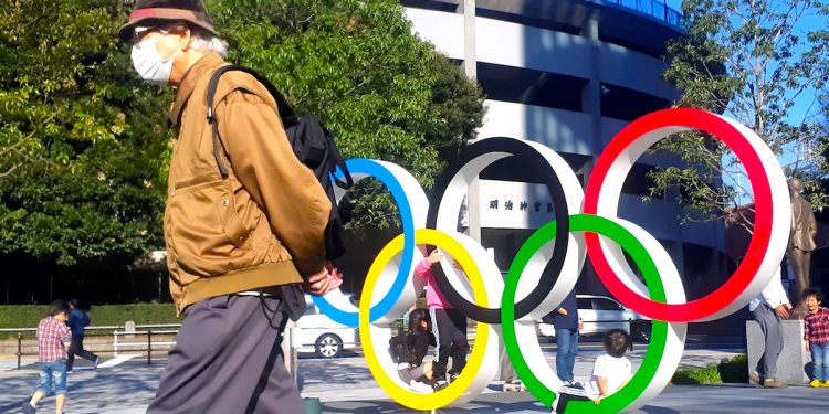 Un hombre protegido por una máscara para evitar posibles contagios da la espalda a los anillos olímpicos instalados en Tokio. EFE/DemÛfilo Pel·ez
