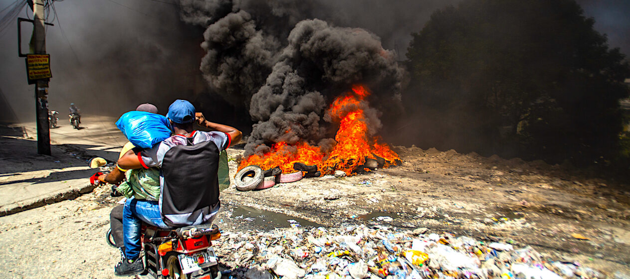 Fotografía de archivo del 19 de  agosto de 2024 de dos hombres se movilizan en motocicleta frente a una barricada con fuego durante una protesta en el barrio Solino, en Puerto Principe (Haití). El Gobierno de Jamaica anunció que da inicio al envío de un número limitado de tropas a la fuerza multinacional, liderada por Kenia, que está desplegada en Haití para restaurar la seguridad. EFE/ Mentor David Lorens