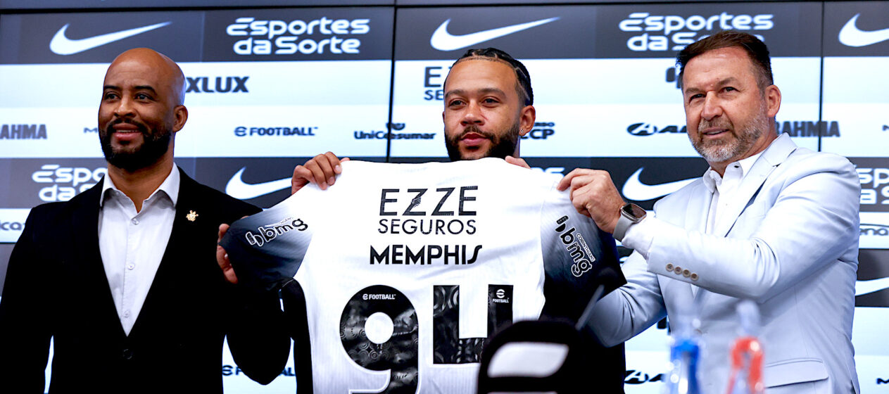 El futbolista neerlandés Memphis Depay (c), sostiene la camisa del Corinthians durante su presentación como nuevo jugador del club acompañado del presidente del Corinthians Augusto Melo (d) y el manager Fabio Soldado (i), durante una rueda de prensa este jueves en el estadio Neo Química Arena, sede del club Corinthians en Sao Paulo (Brasil). Depay fue recibido como una estrella en el aeropuerto internacional de Guarulhos, en São Paulo, por la afición del Corinthians, en un momento en que el equipo lucha por no descender a segunda división. EFE/ Sebastião Moreira