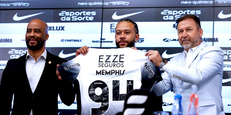 El futbolista neerlandés Memphis Depay (c), sostiene la camisa del Corinthians durante su presentación como nuevo jugador del club acompañado del presidente del Corinthians Augusto Melo (d) y el manager Fabio Soldado (i), durante una rueda de prensa este jueves en el estadio Neo Química Arena, sede del club Corinthians en Sao Paulo (Brasil). Depay fue recibido como una estrella en el aeropuerto internacional de Guarulhos, en São Paulo, por la afición del Corinthians, en un momento en que el equipo lucha por no descender a segunda división. EFE/ Sebastião Moreira