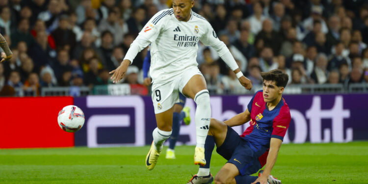 El delantero del Real Madrid Kylian Mbappé (i) lucha con Pau Cubarsí, del FC Barcelona, durante el partido de la jornada 11 de LaLiga EA Sports entre el Real Madrid y el FC Barcelona, este sábado en el estadio Santiago Bernabéu, en Madrid. EFE/Juanjo Martín