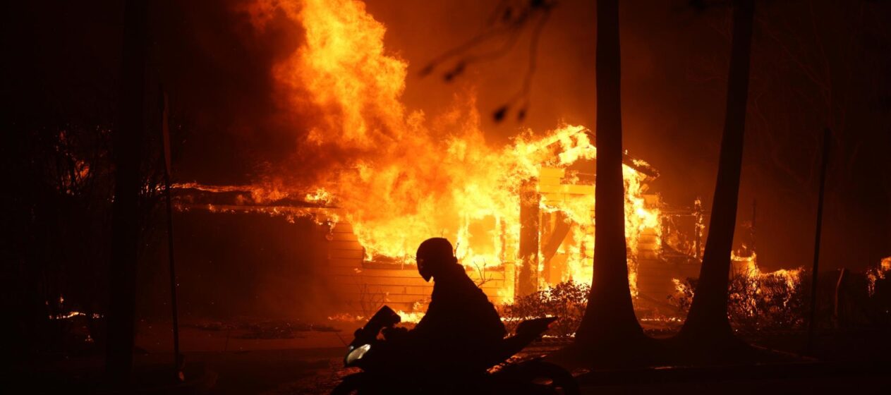 -FOTODELDIA- Los Ángeles (Estados Unidos), 08/01/2025.- Una persona conduce su motocicleta junto a una casa en llamas durante los incendios en Palisades , California, Estados Unidos. Dos incendios avanzan sin control alentados por fuertes vientos que mantienen en estado de emergencia a una parte de Los Ángeles, con 30.000 personas evacuados y la amenaza de que las llamas se sigan propagando rápidamente por zonas de viviendas. EFE/ Allison Dinner