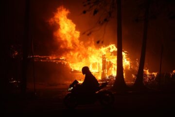 -FOTODELDIA- Los Ángeles (Estados Unidos), 08/01/2025.- Una persona conduce su motocicleta junto a una casa en llamas durante los incendios en Palisades , California, Estados Unidos. Dos incendios avanzan sin control alentados por fuertes vientos que mantienen en estado de emergencia a una parte de Los Ángeles, con 30.000 personas evacuados y la amenaza de que las llamas se sigan propagando rápidamente por zonas de viviendas. EFE/ Allison Dinner